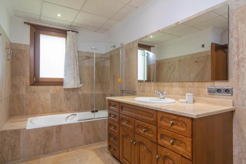 A bathroom with a bathtub, glass shower screen, and wooden vanity.