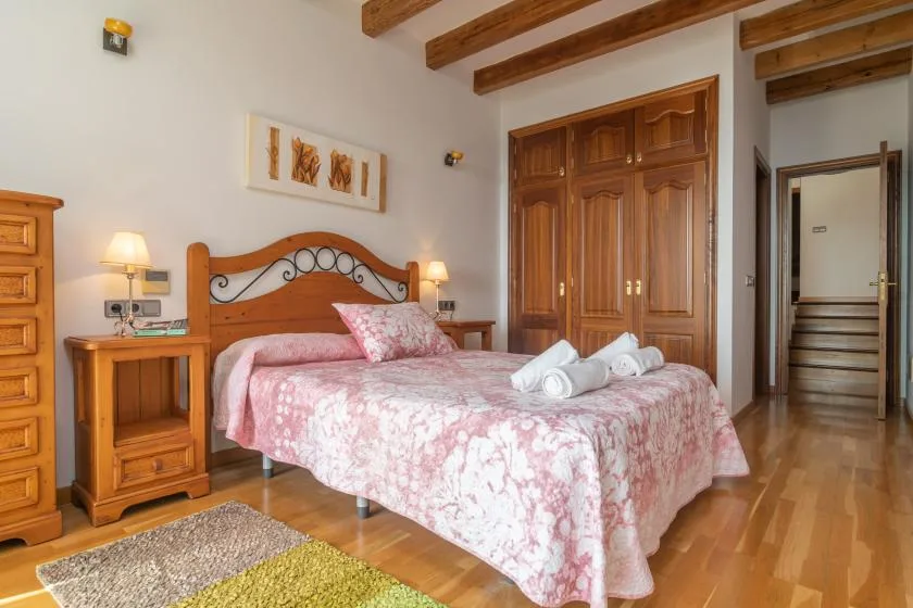 A bedroom with a wooden bed, pink floral bedding, and exposed ceiling beams.