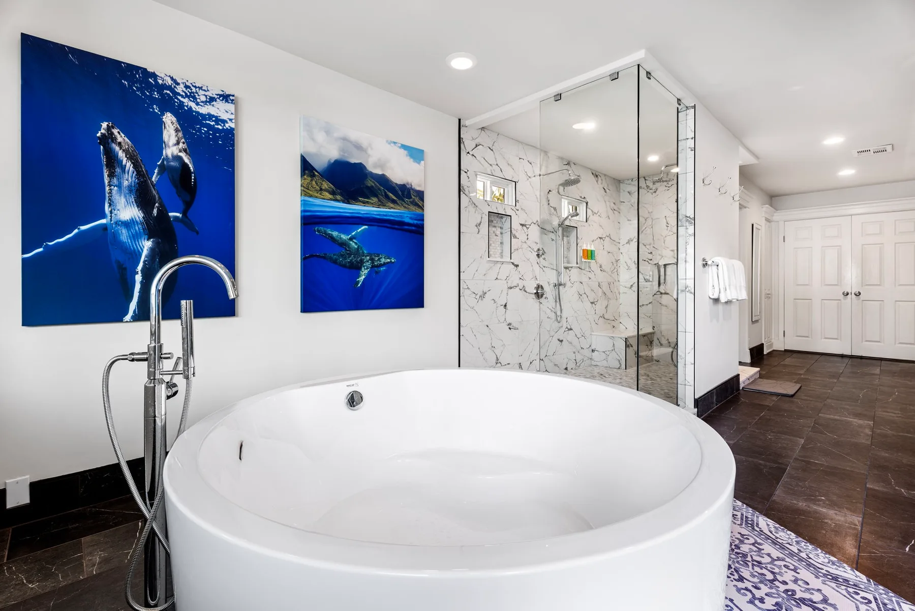 Un baño con una bañera amplia, ducha de cristal y cuadros de temática oceánica.