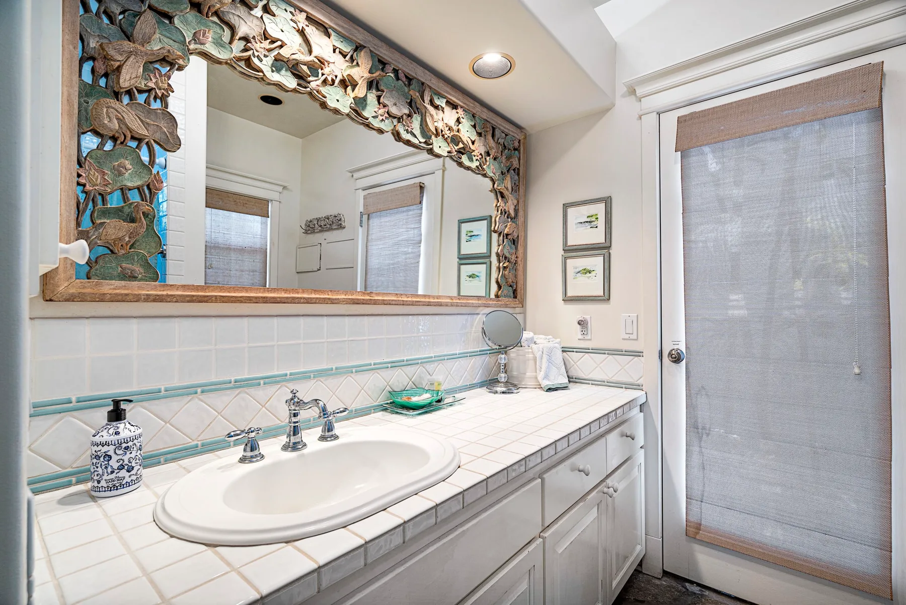 Un baño luminoso con tocador de azulejos, lavabo y un gran espejo enmarcado.
