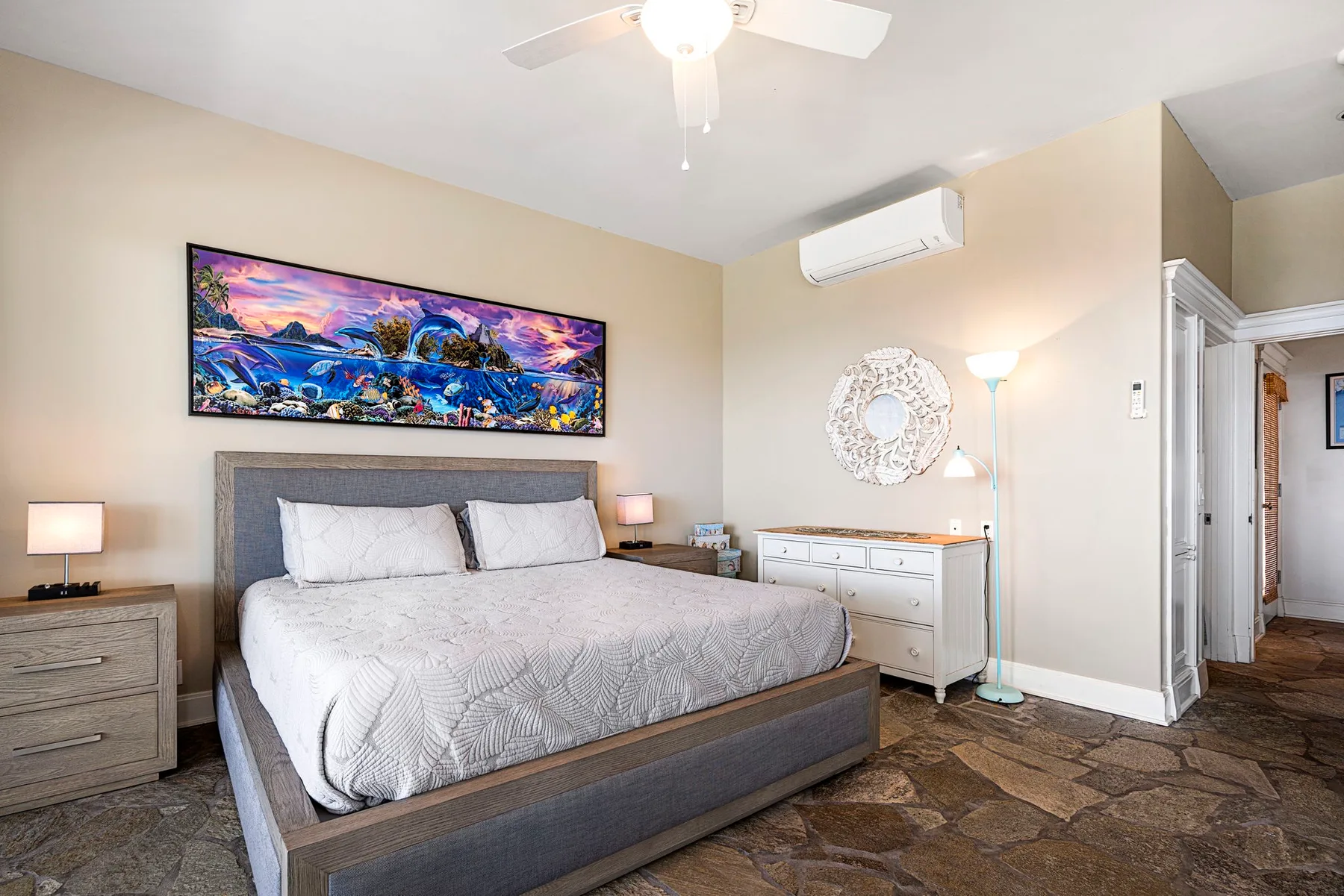 Un dormitorio con una cama, arte colorido en la pared y una cómoda.