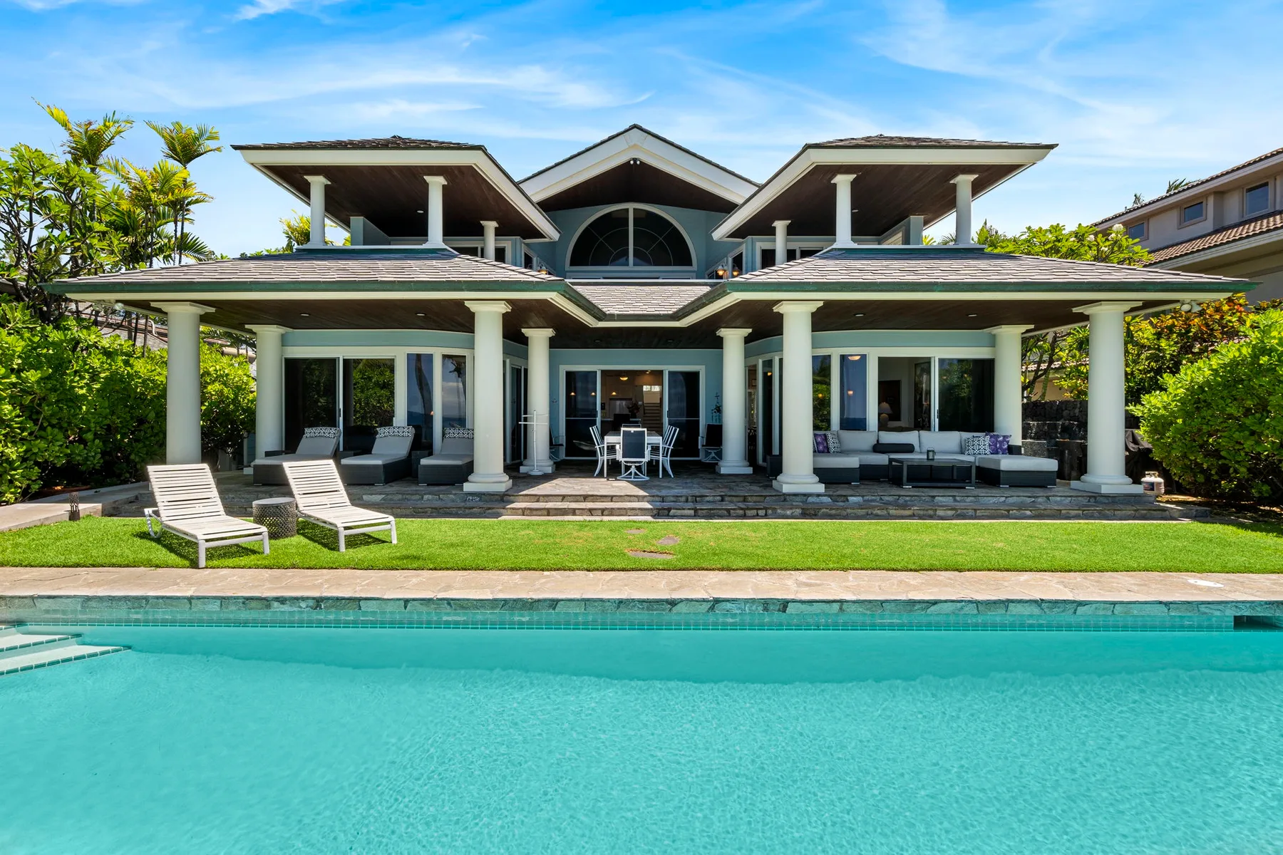 Una casa grande con patio cubierto y piscina al frente.