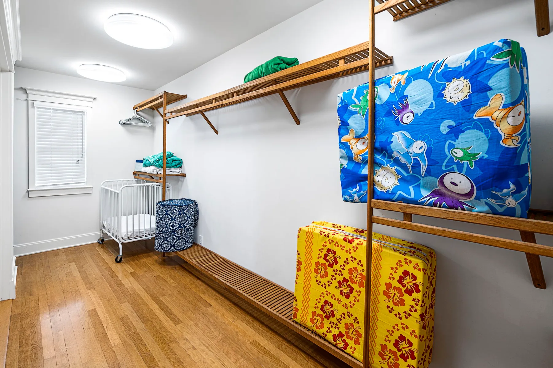 Un cuarto de almacenamiento con estantes de madera en la pared, ropa de cama doblada y una cuna.