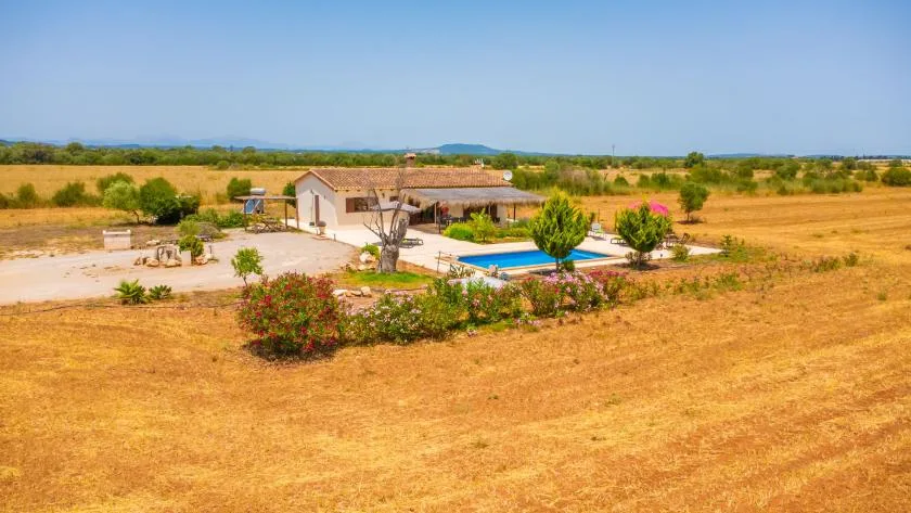A low house and swimming pool sit among dry fields and scattered shrubs.