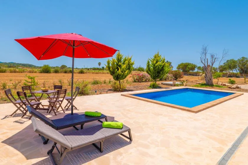 A swimming pool and sun loungers sit on a patio beneath a red umbrella.