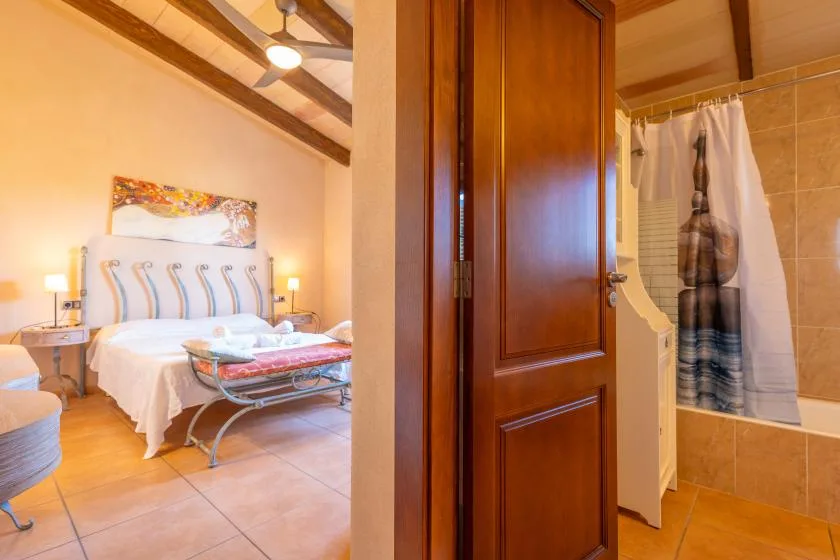 A bedroom with a bed and an adjoining bathroom visible through an open doorway.