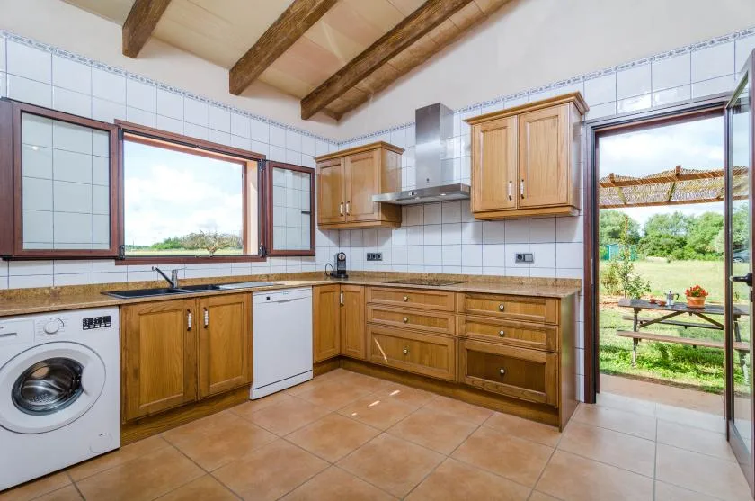 A tiled kitchen with wooden cabinets, a countertop, and a view of the garden.