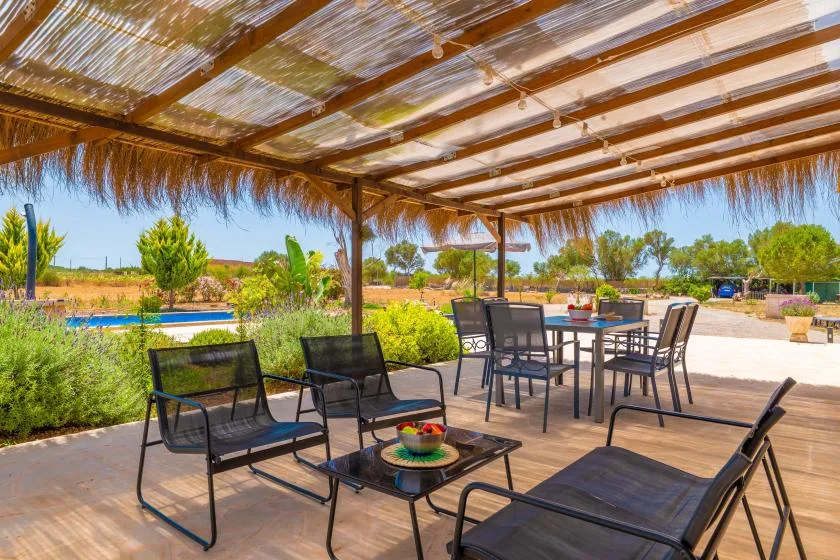 A covered outdoor patio with seating and a table overlooks a landscaped pool area.