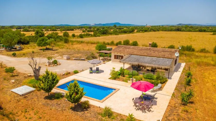 A swimming pool and patio sit beside a small building in an open rural landscape.
