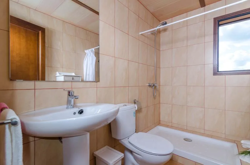 A tiled bathroom with a sink, toilet, and bathtub beneath a window.