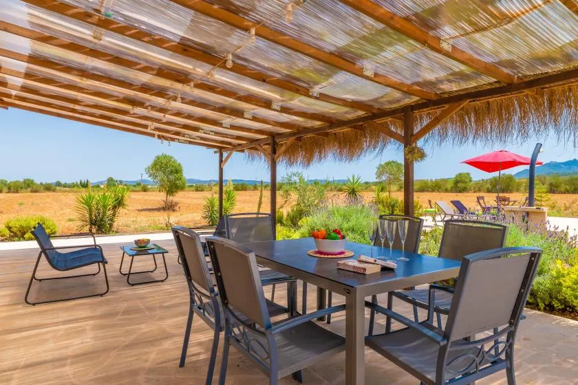 An outdoor dining area beneath a shaded pergola overlooks an open field.