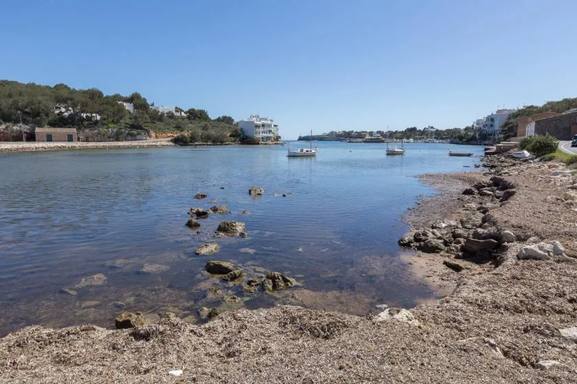 A calm coastal inlet with boats on the water and a rocky shoreline.