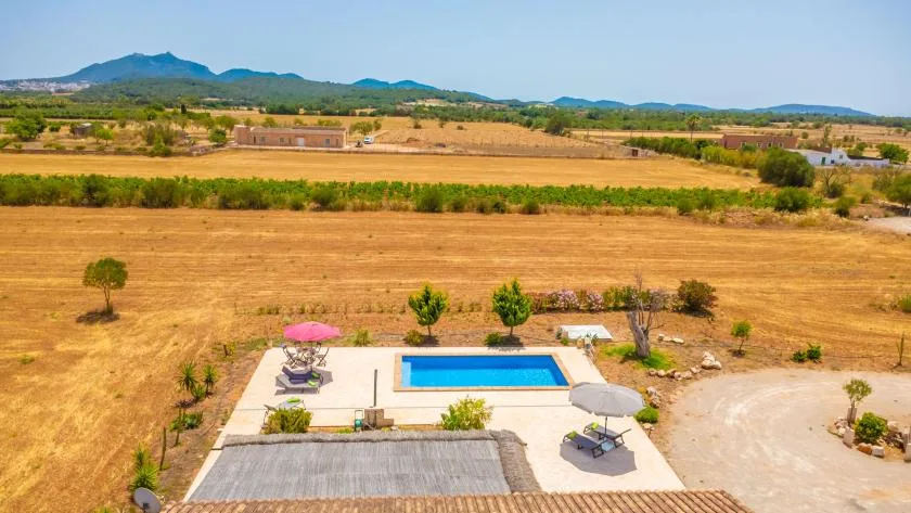 Aerial view of a swimming pool and patio beside dry fields and distant hills.