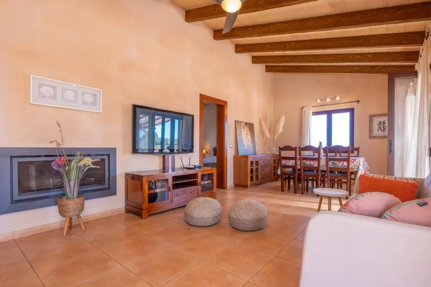 A living and dining room with a television, dining table, and exposed ceiling beams.