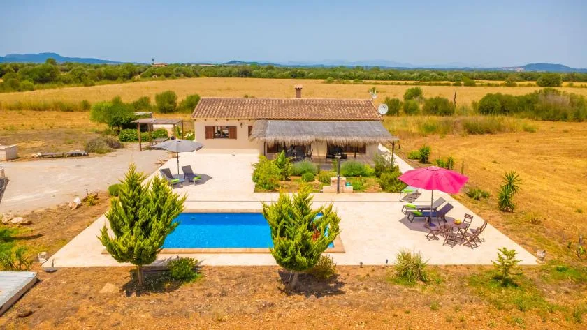 A rural house and swimming pool sit amid open fields and dry countryside.