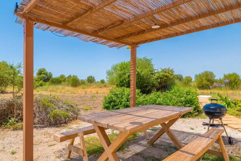 A picnic table sits beneath a shaded wooden pergola in a sunny garden.