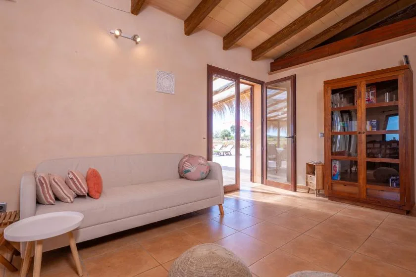 A living room with a sofa, wooden ceiling beams, and glass doors opening to a patio.