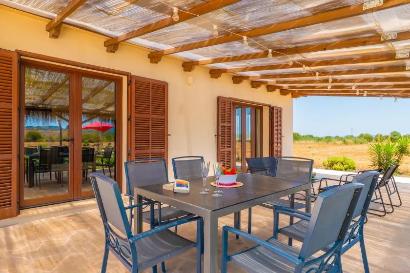 A covered outdoor dining area with a table and chairs overlooks open greenery.