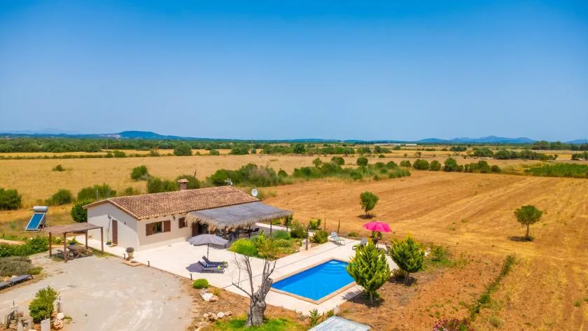 A house and swimming pool sit amid open, dry fields under a clear sky.