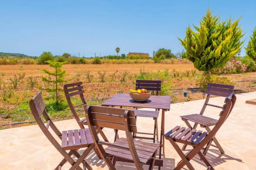 An outdoor patio with wooden seating and a table overlooks a dry field.