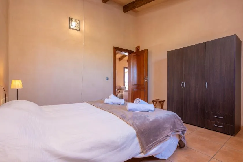 A bedroom with a bed, a dark wardrobe, and an open wooden door.