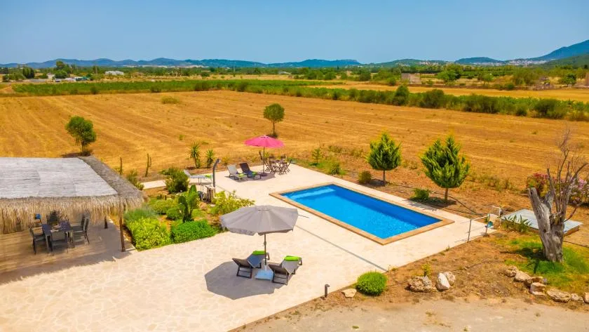 A swimming pool and patio sit beside open fields and distant hills.