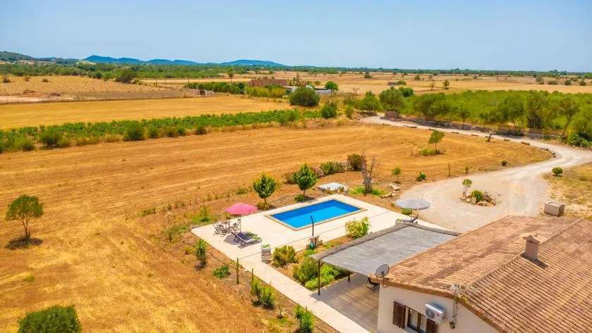 An aerial view shows a swimming pool beside a house in a dry rural landscape.