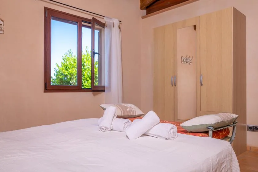 A bedroom with a bed and a wooden wardrobe beside the window.