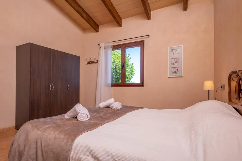A bedroom with a bed, dark wardrobe, and a window overlooking greenery.