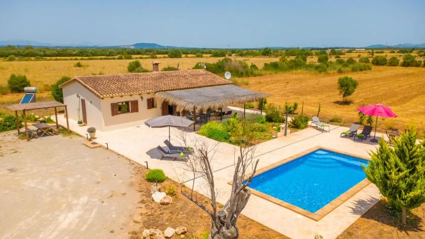 A rural house and swimming pool sit amid open fields under a clear sky.