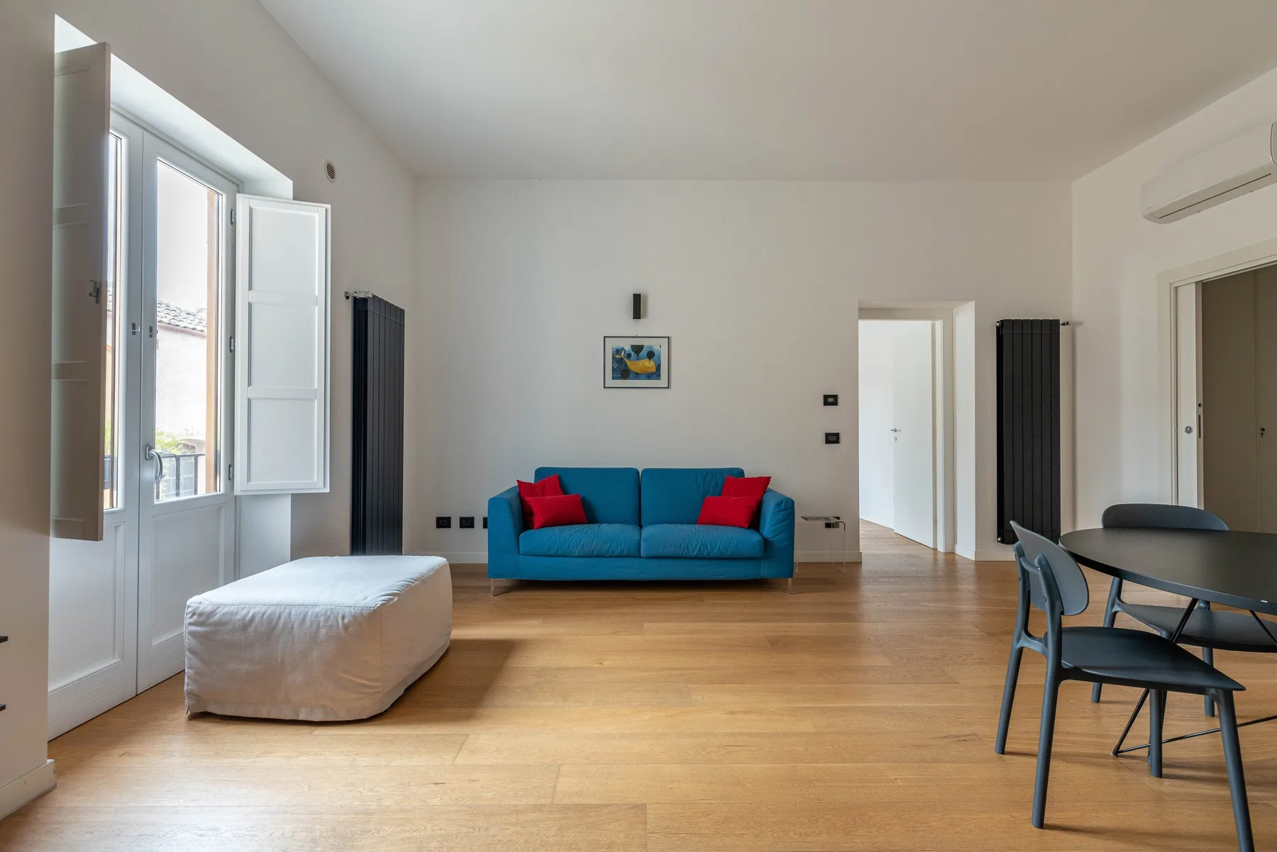A bright living room with blue seating, a dining table, and open windows.