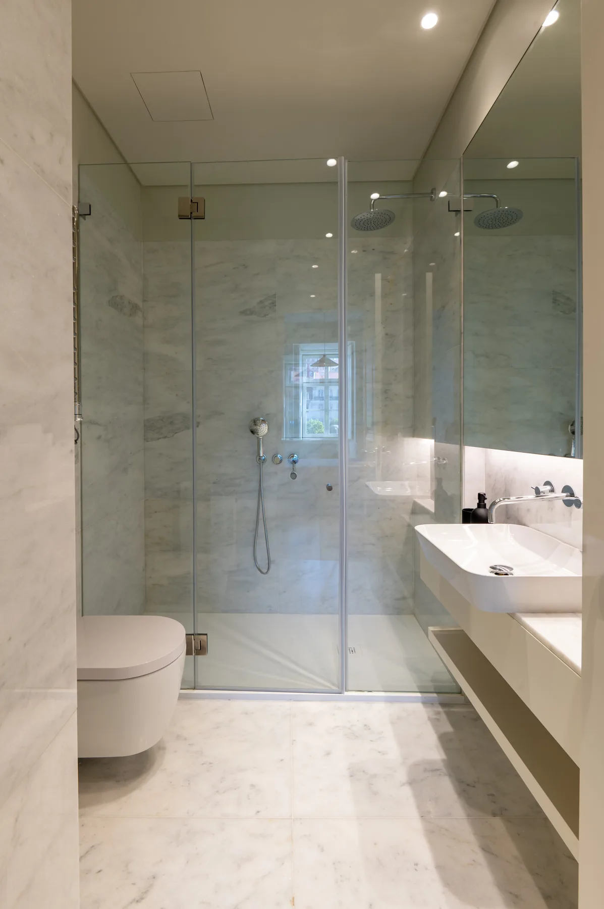 Un baño luminoso con ducha de cristal y lavabo suspendido.