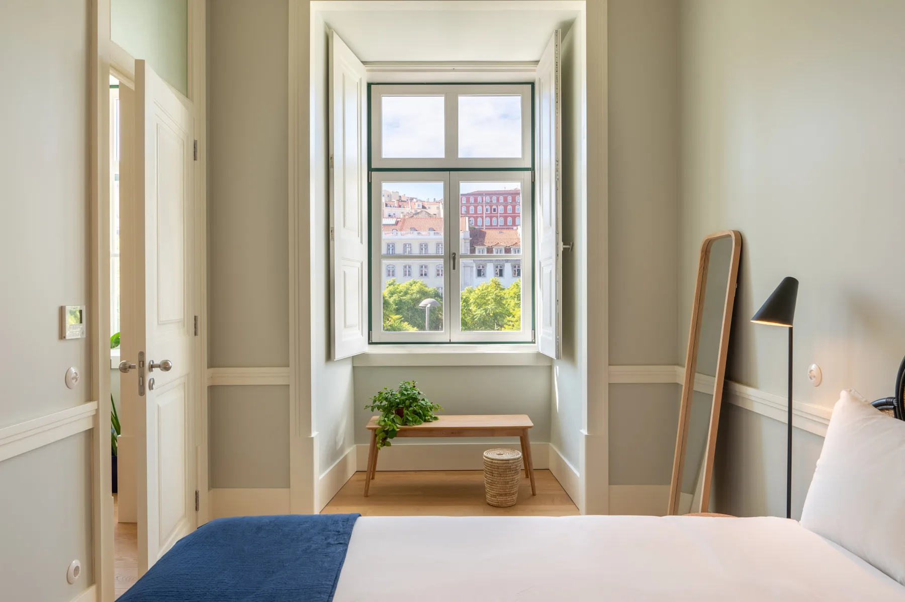 A bedroom with a large window, a small bench, and a bed.