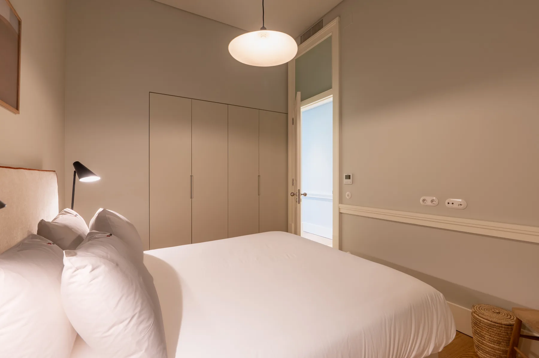 Un dormitorio con una cama bien hecha, un armario empotrado y una lámpara colgante.