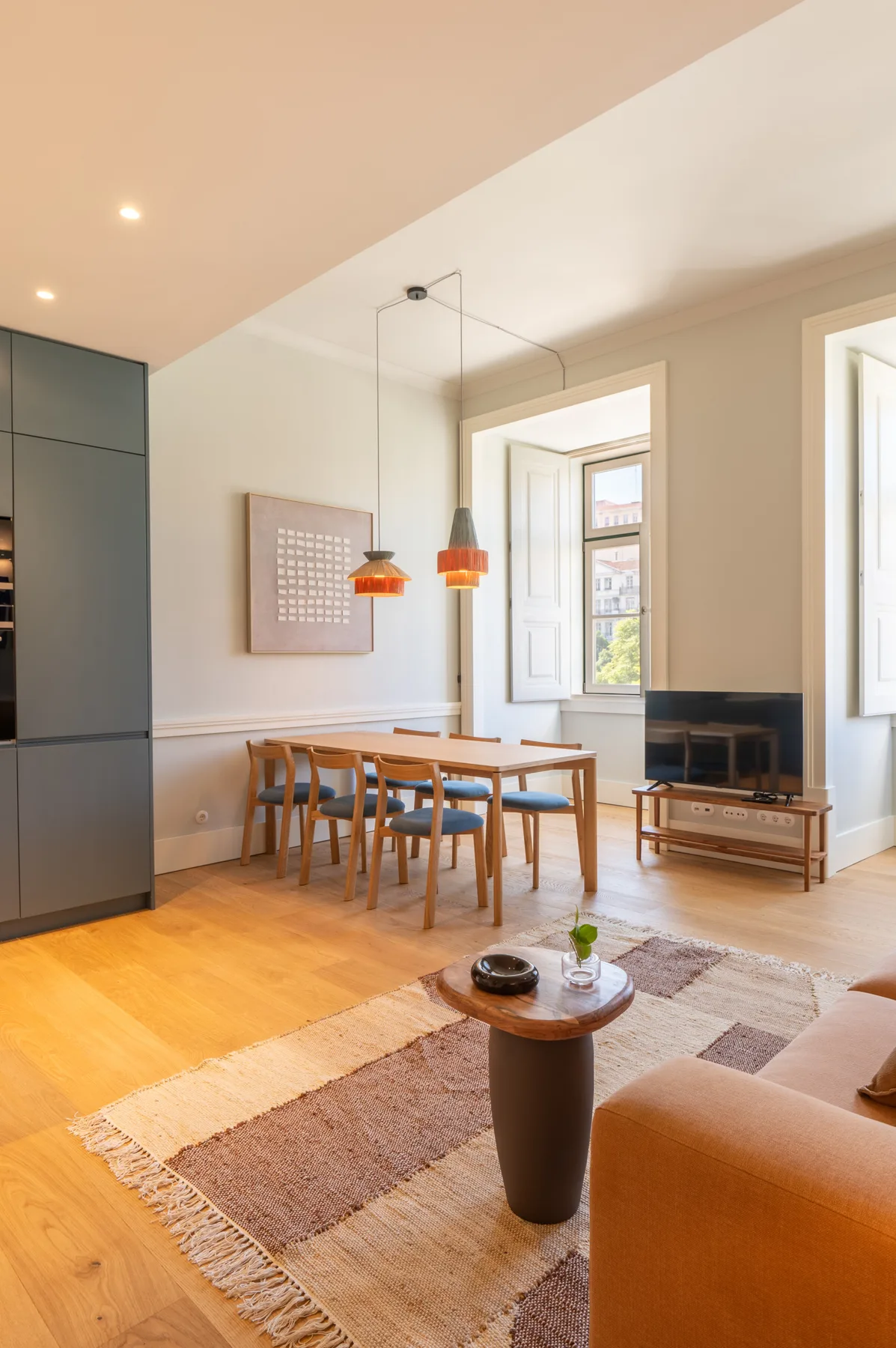 A bright living and dining area with a wooden table, seating, and a rug.