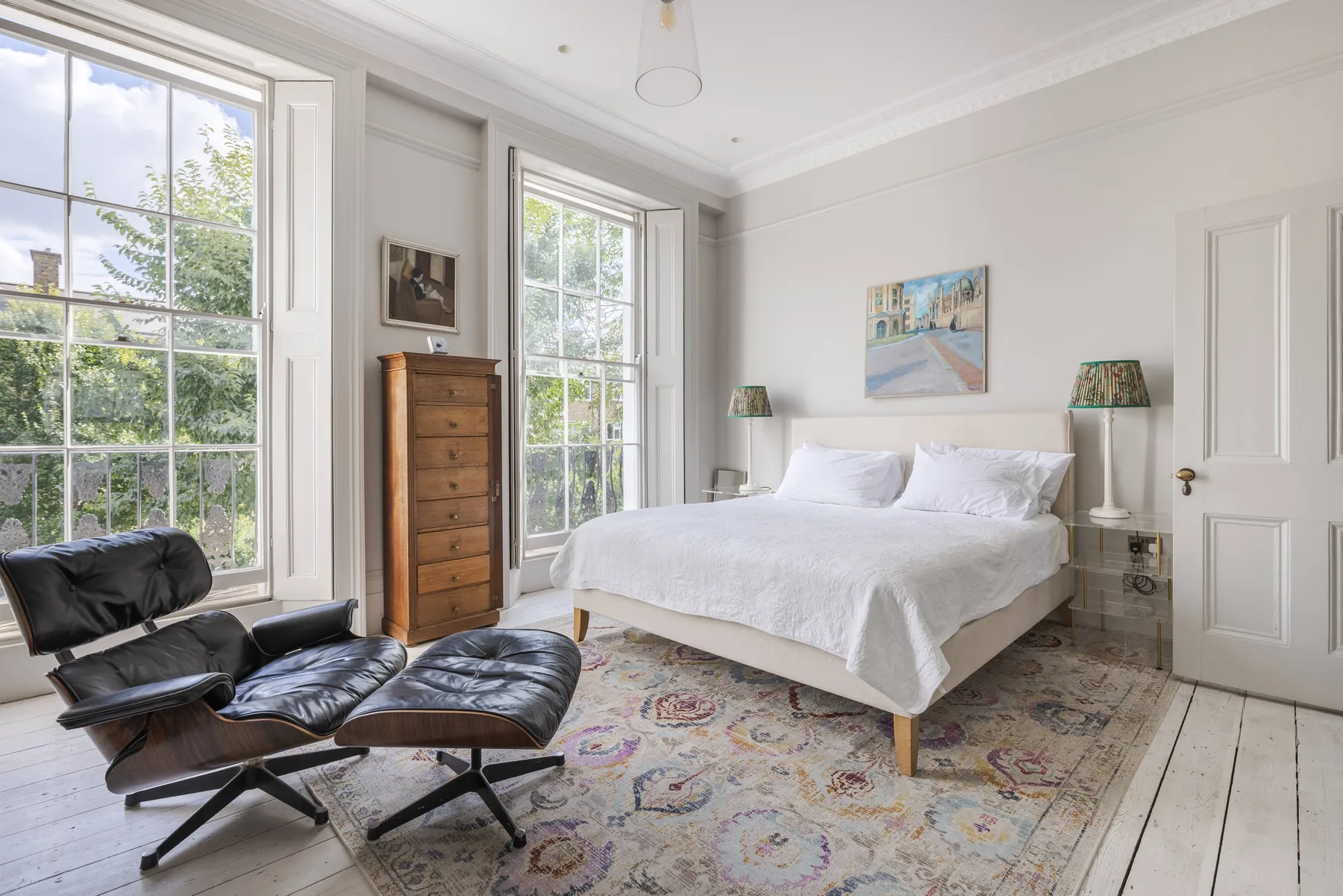 A bright bedroom with a white bed, large windows, and a patterned rug.