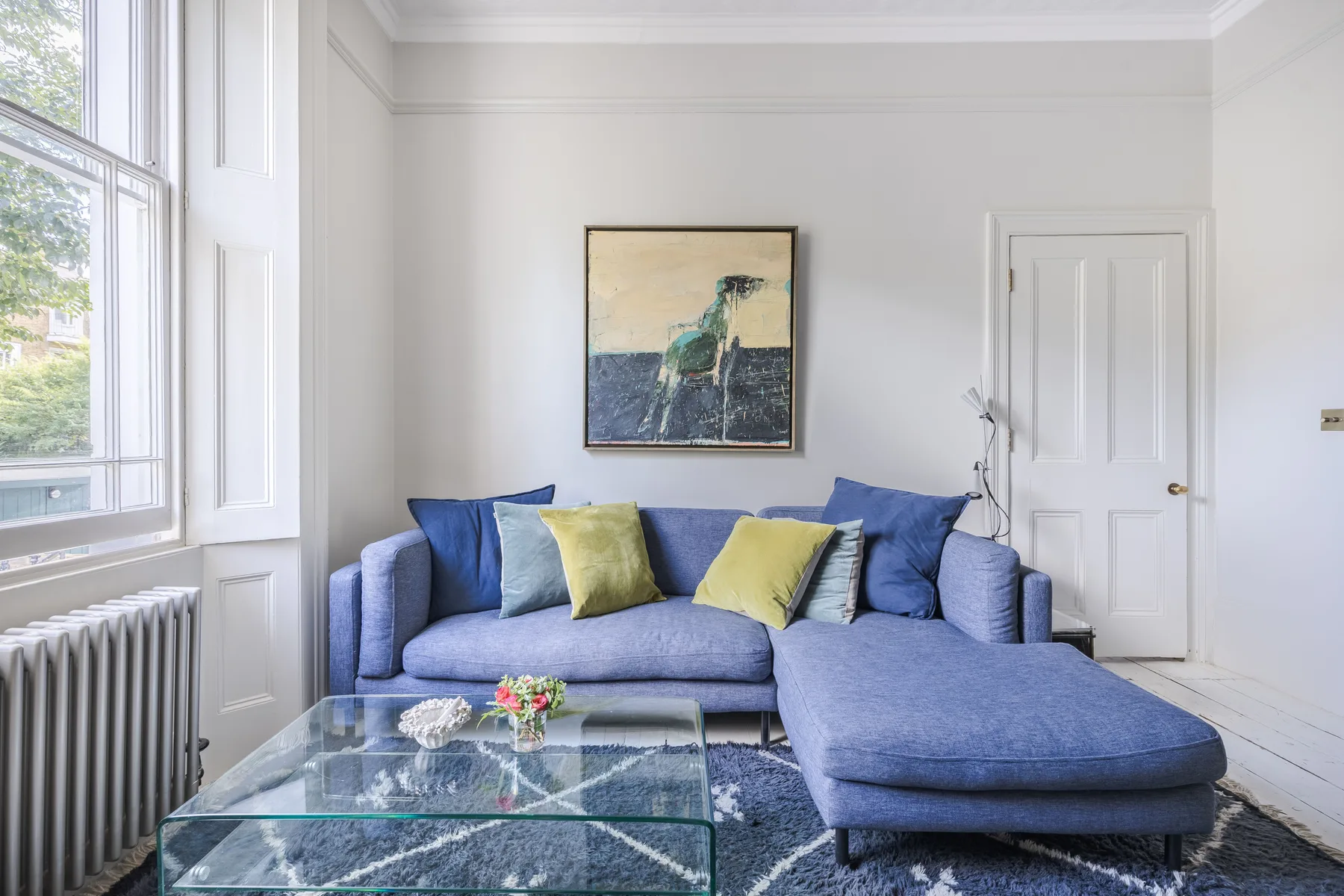 Una sala luminosa con asientos azules, una mesa de centro de vidrio y ventanas altas.