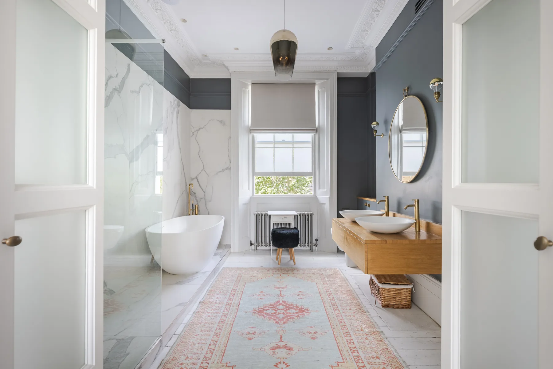 Un baño luminoso con bañera exenta, lavabo con mueble y una ventana.