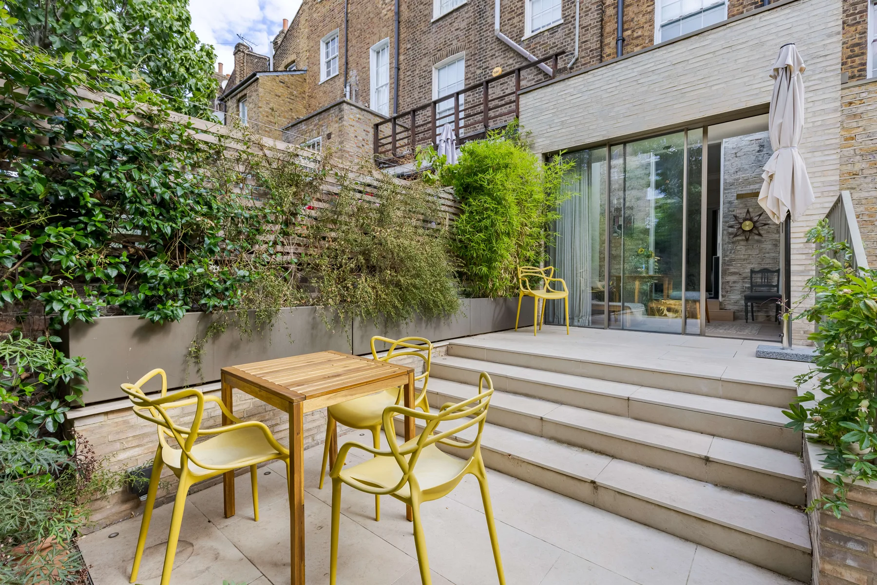 Un patio pavimentado con asientos amarillos, una mesa de madera y puertas de vidrio.