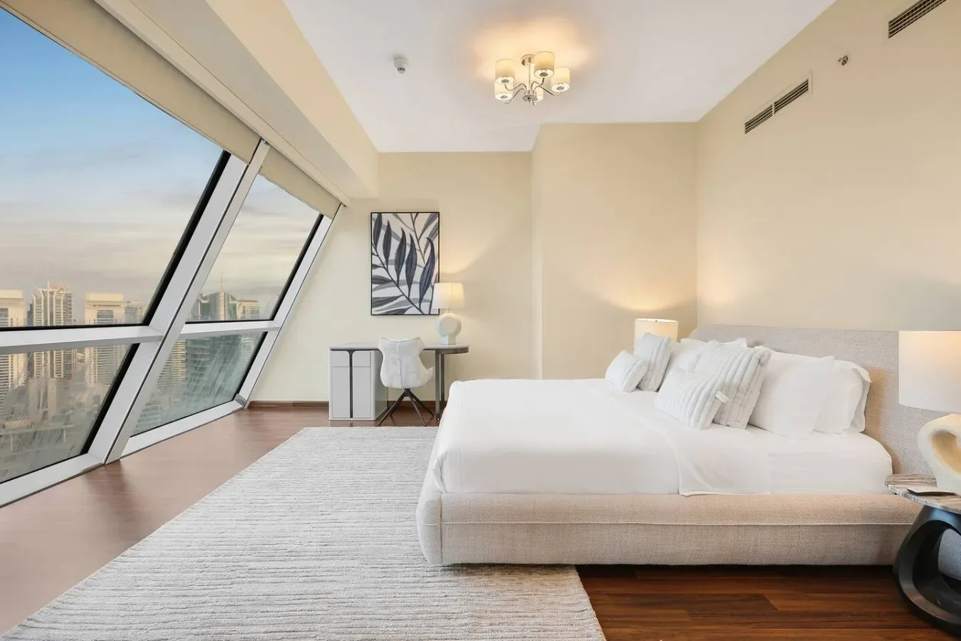 Un dormitorio luminoso con una cama grande junto a ventanas inclinadas con vistas a la ciudad.