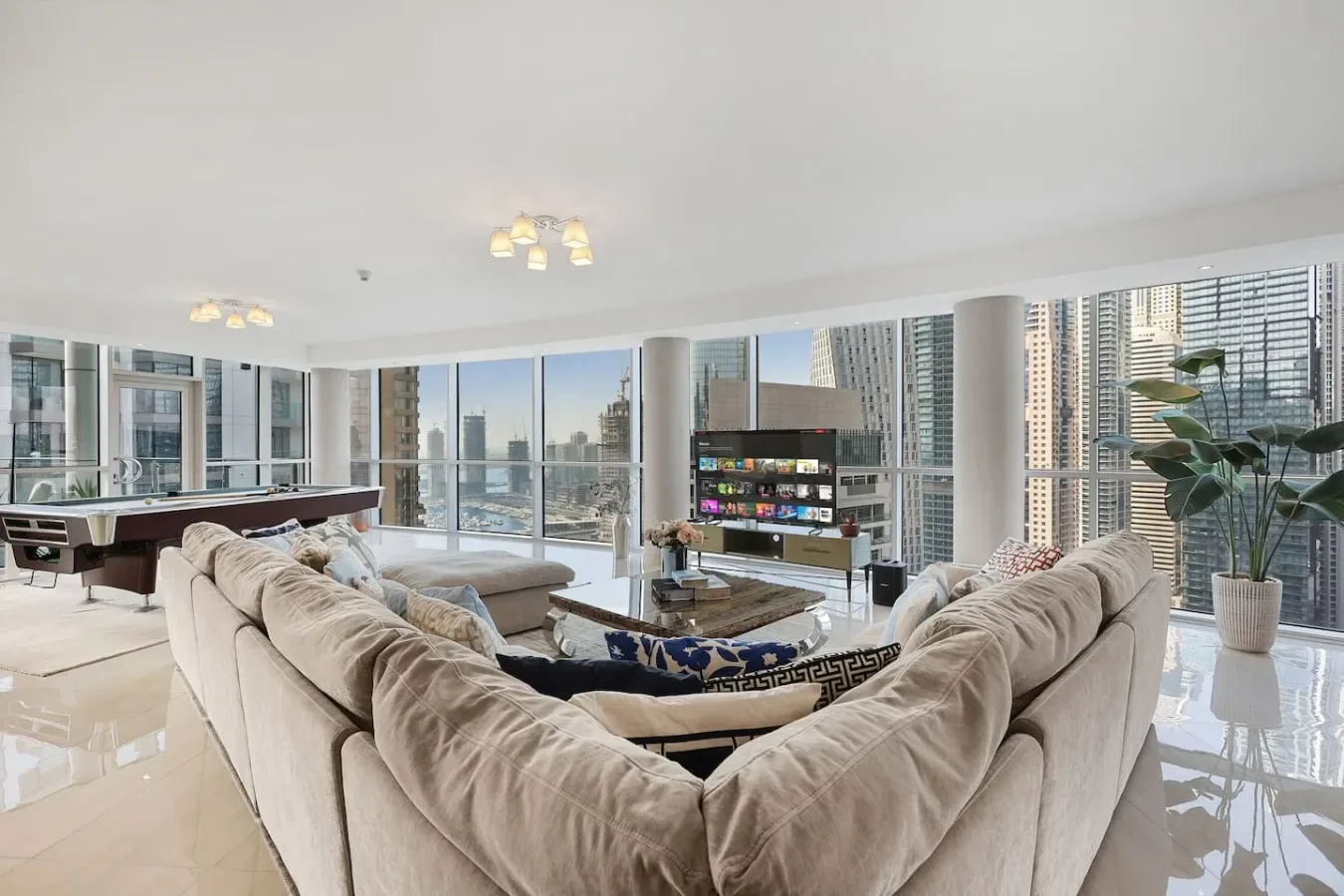 A bright living room with curved seating and floor-to-ceiling windows overlooking city buildings.