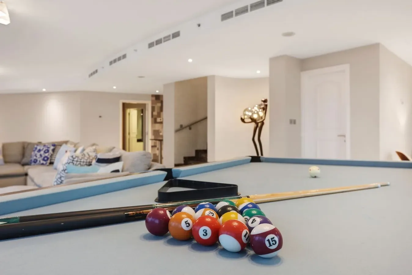 A pool table with colorful balls sits in a bright basement lounge.