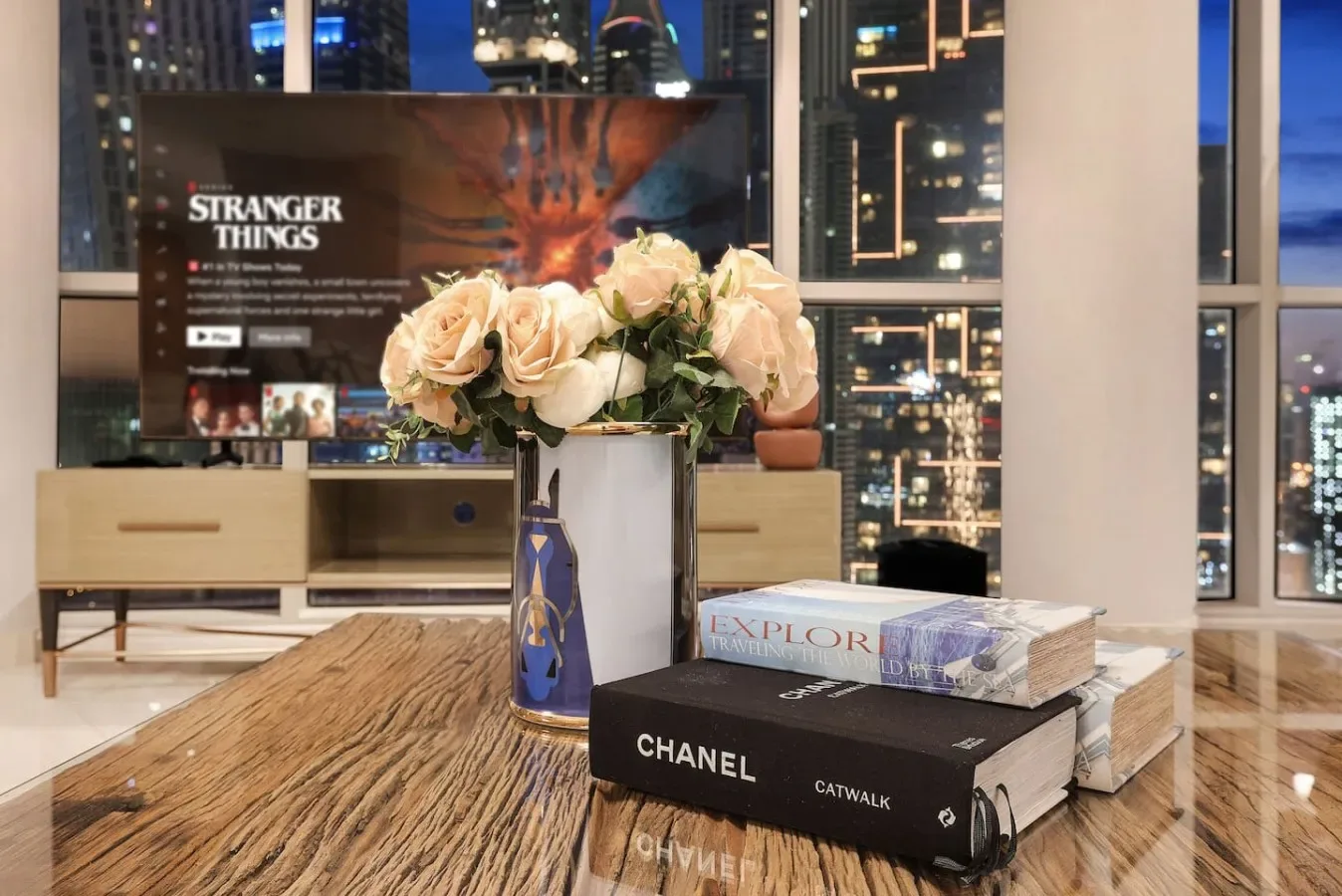A living room with flowers displayed on a coffee table in front of city-view windows.