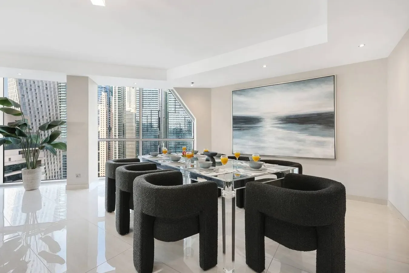 Un comedor luminoso con asientos oscuros alrededor de una mesa de vidrio junto a grandes ventanas.