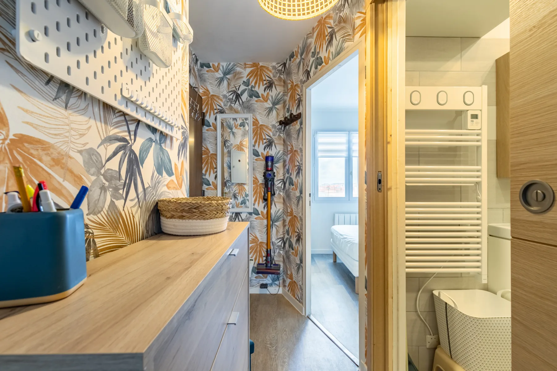 A compact bathroom with a vanity, patterned walls, and a shower area.