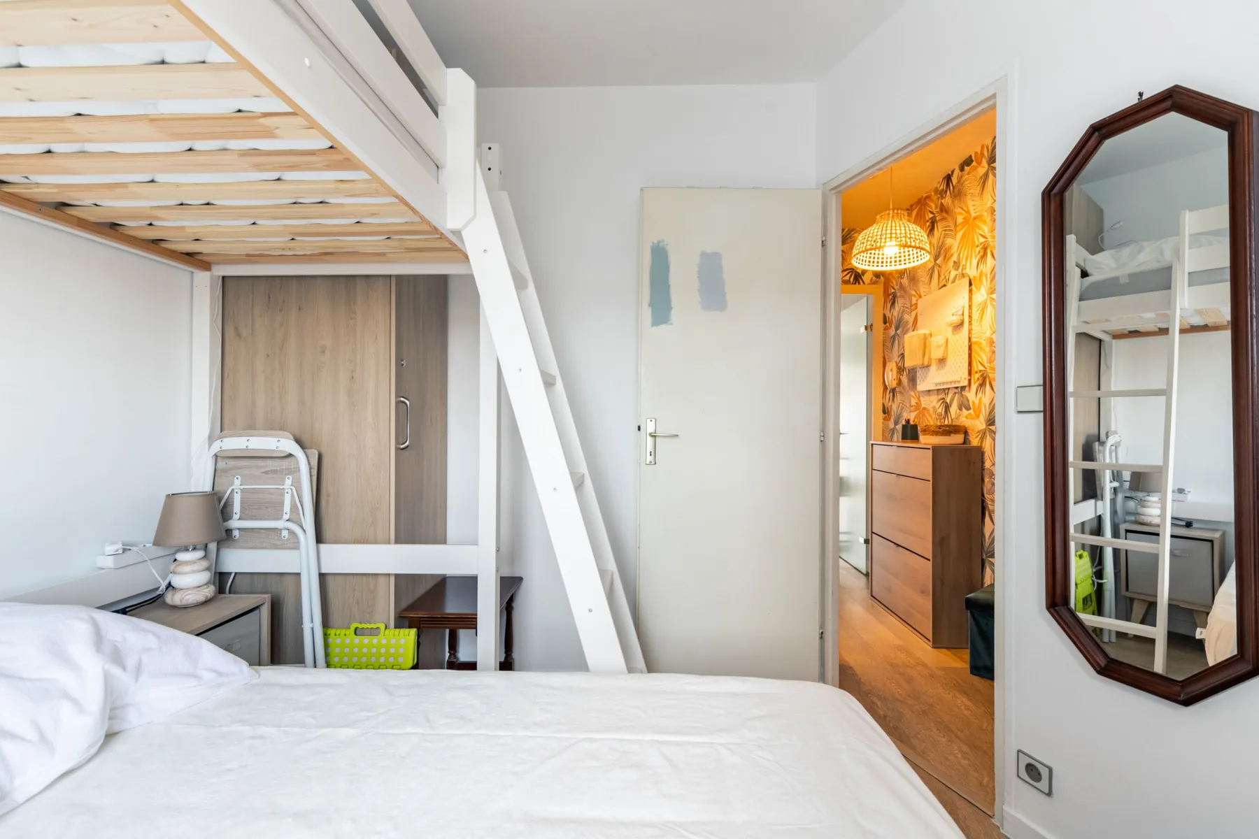 A bedroom with a loft bed, a sleeping area, and a doorway to a warmly lit room.