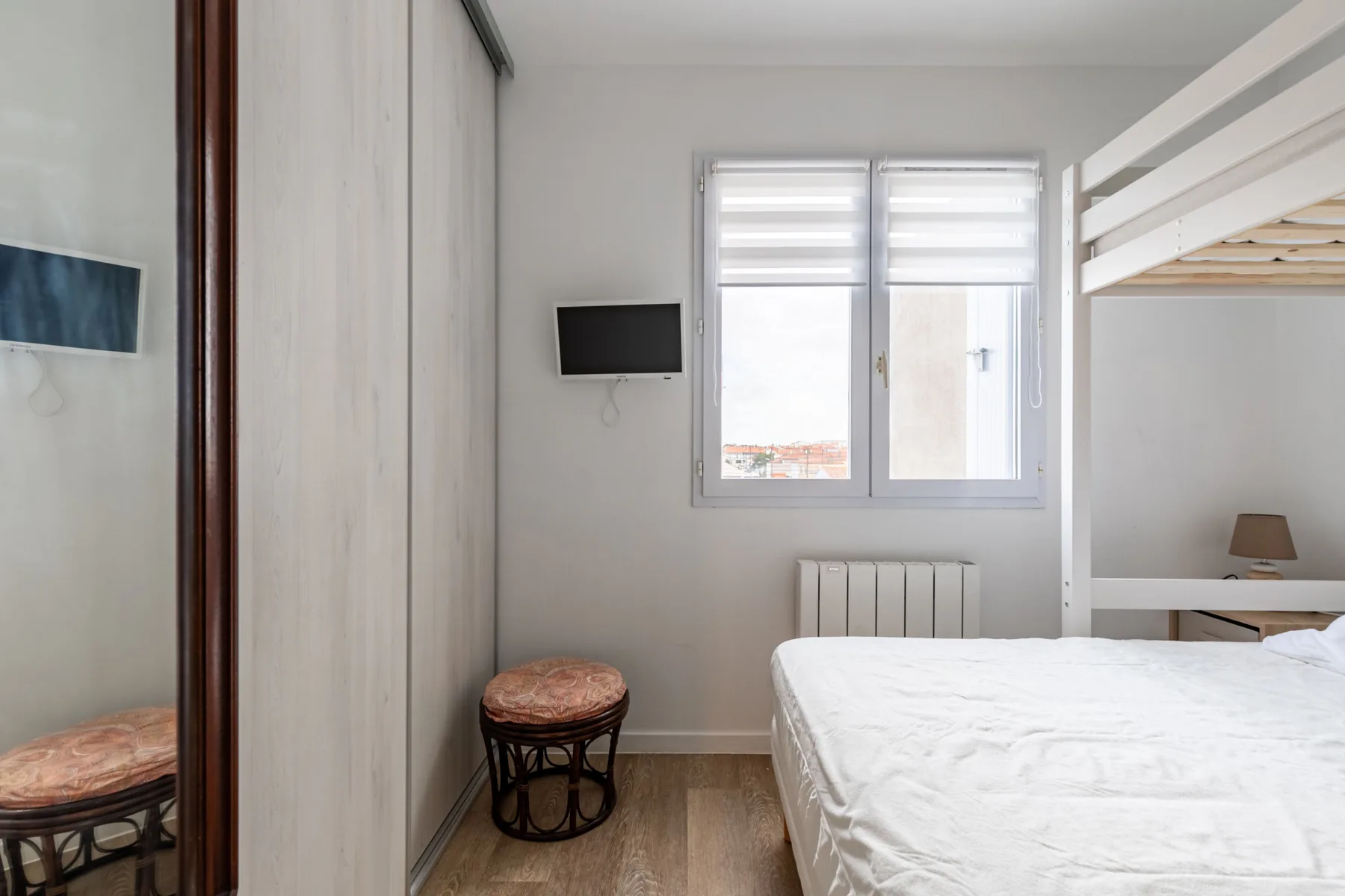 A bright bedroom with a bed, a window, and a wall-mounted television.