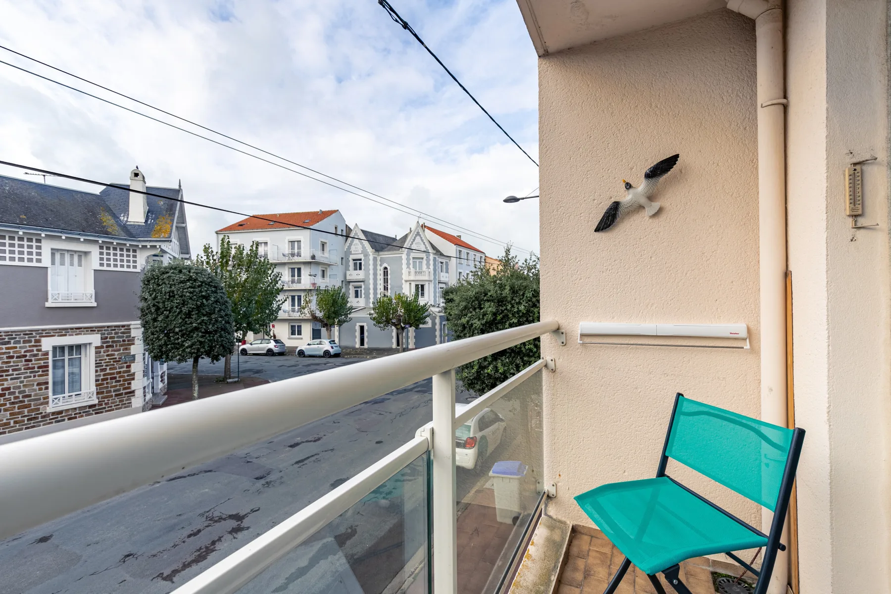 A small balcony overlooks a residential street, with a turquoise chair beside the railing.