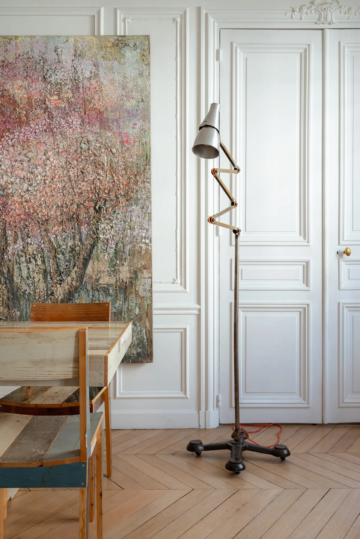 A paneled room with a large floral painting, a desk, and an adjustable floor lamp.