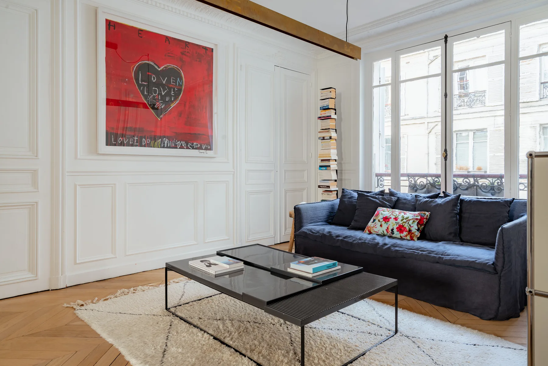 A bright living room has dark seating, a glass coffee table, and large windows.